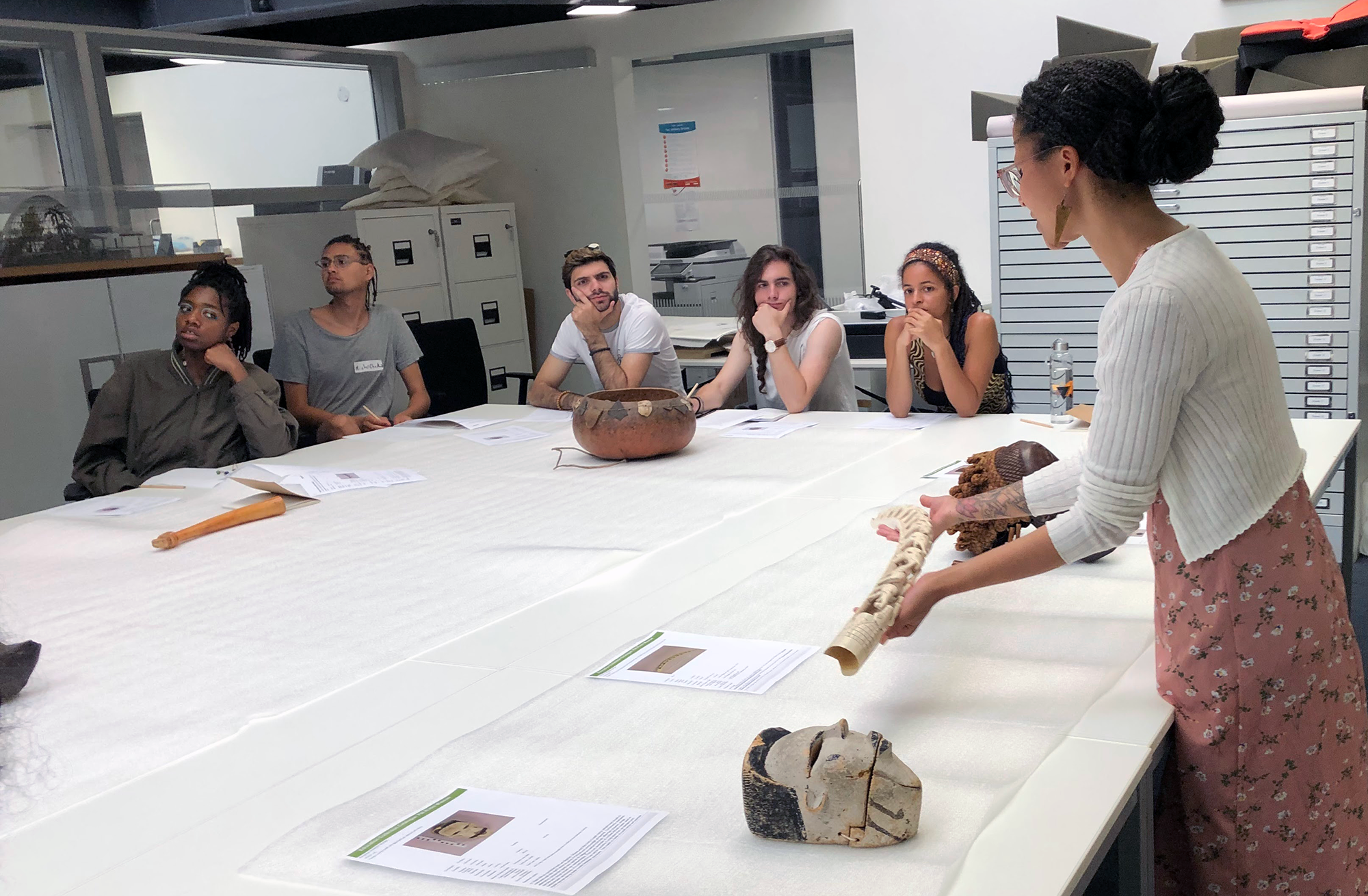 a person shows a carved ivory object to a group of people sat around a table with further museum objects