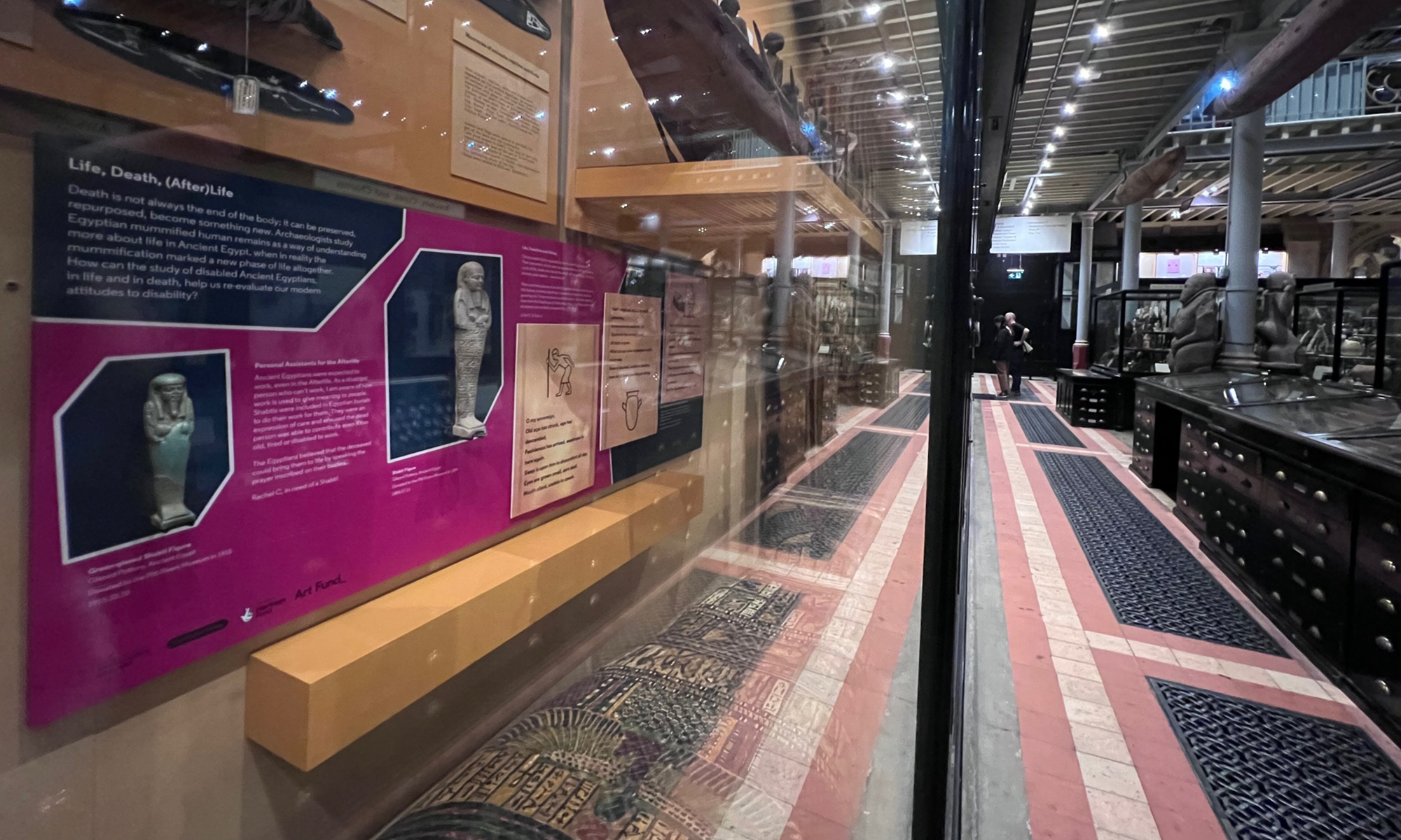 A view of bright pink display graphic in a museum wall case with items from Ancient Egypt