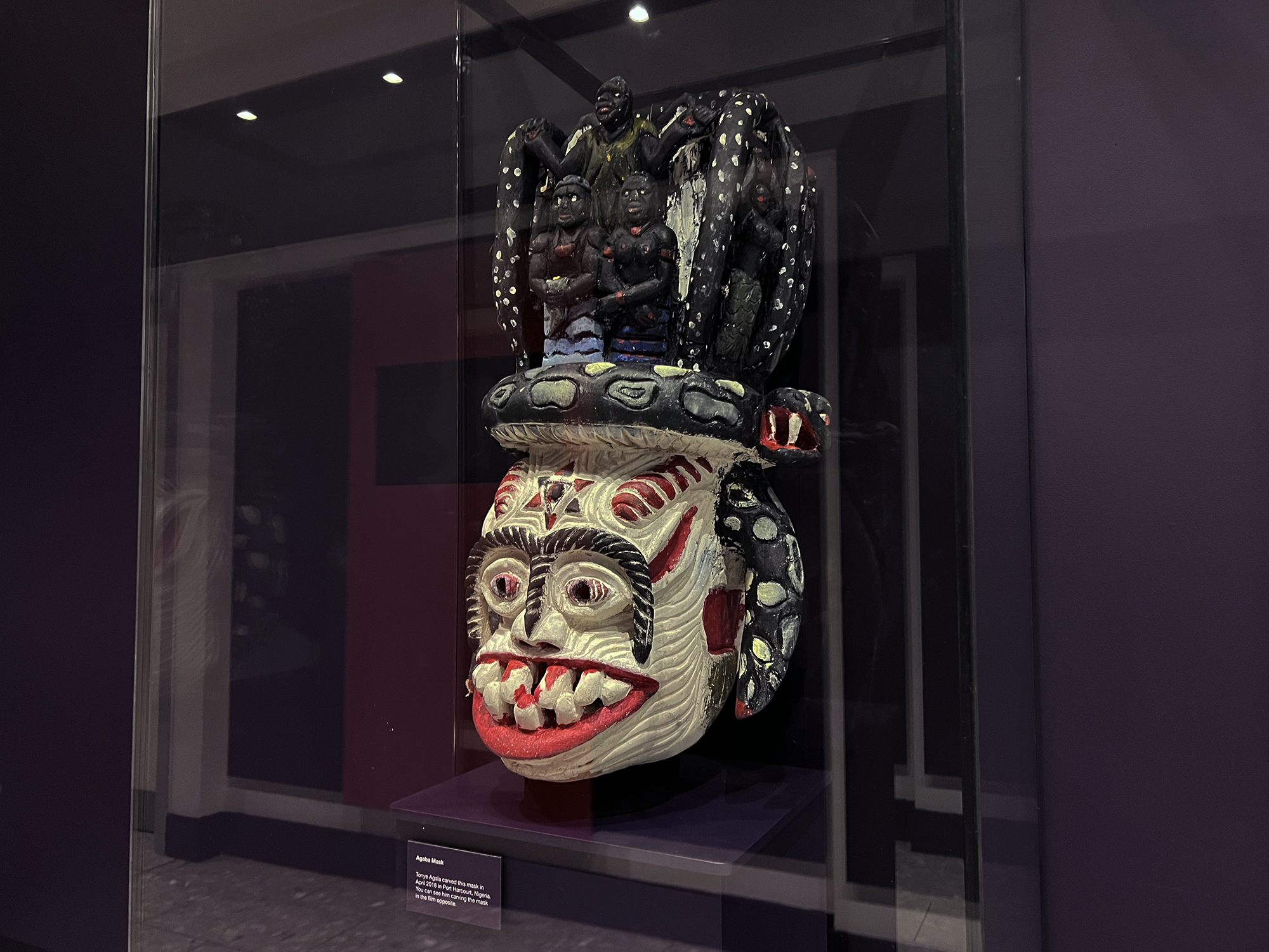 A large wooden mask with a face and the base and carved details included figures above. 