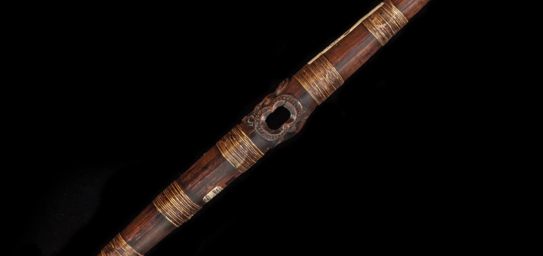 Wooden Pūtōrino or bugle flute with a face carved at both ends and one at the centre.