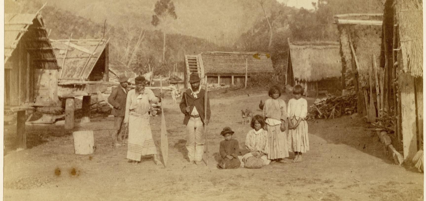 Māori family pictured amidst houses at Pipiriki, a settlement on the Whanganui River. Photograph by Alfred Burton for the Burton Brothers studio (Dunedin). Pipiriki, North Island, New Zealand. 11 May 1885.
