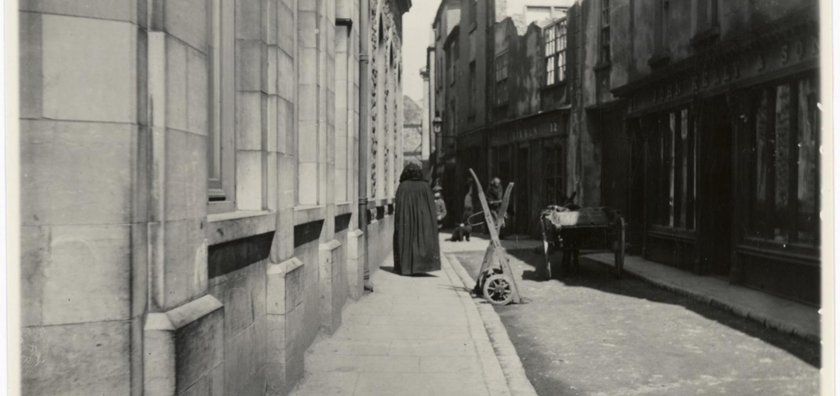 Woman walking in an empty street, wearing a gown with hood for head.