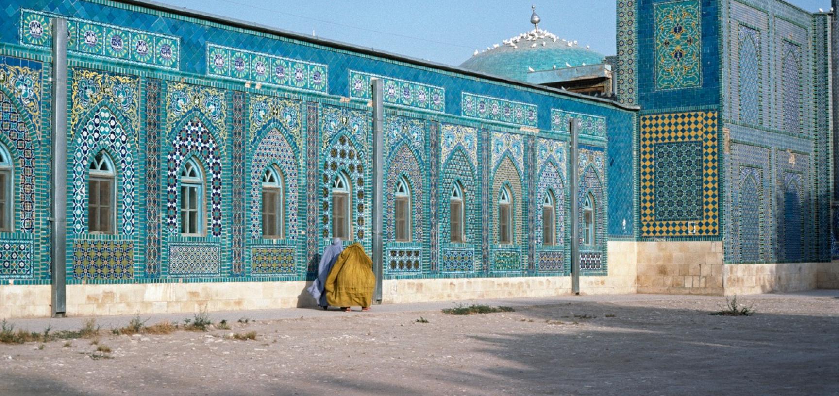 Two women in burqas walking near a brightly decorated blue mosque