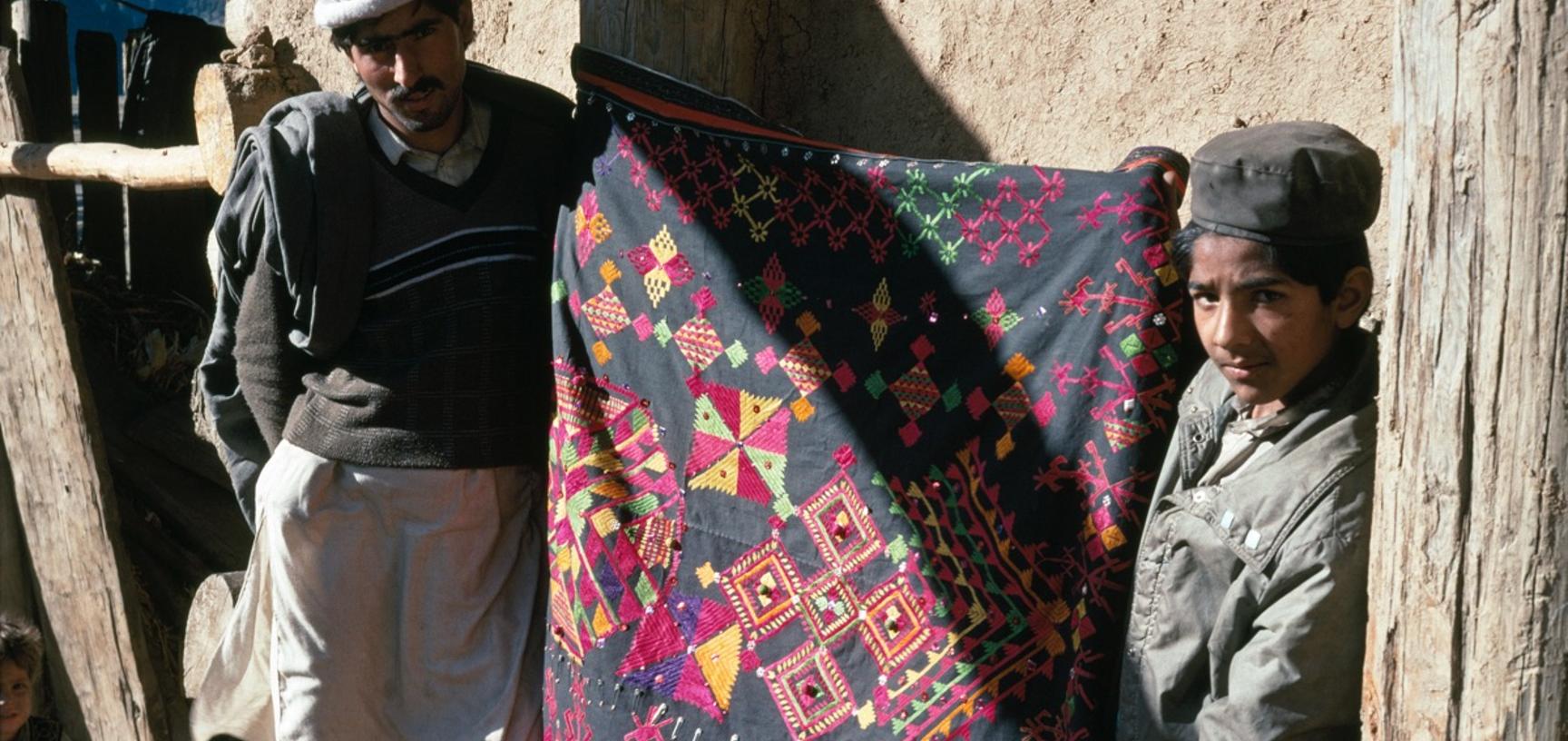 A man and boy holding an embroidered textile, Palas valley, Pakistan.