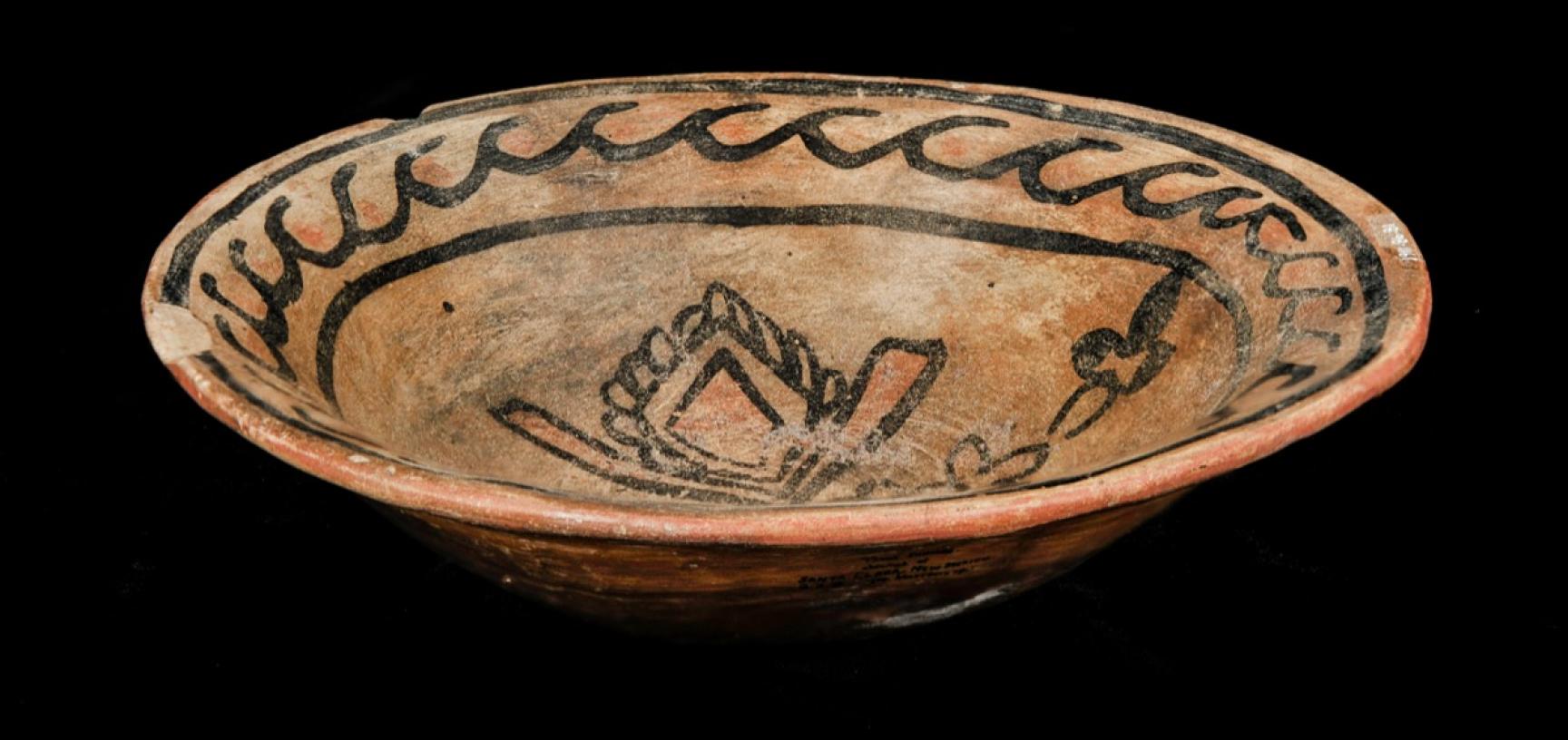 Worn red ceramic bowl with black designs on the inside