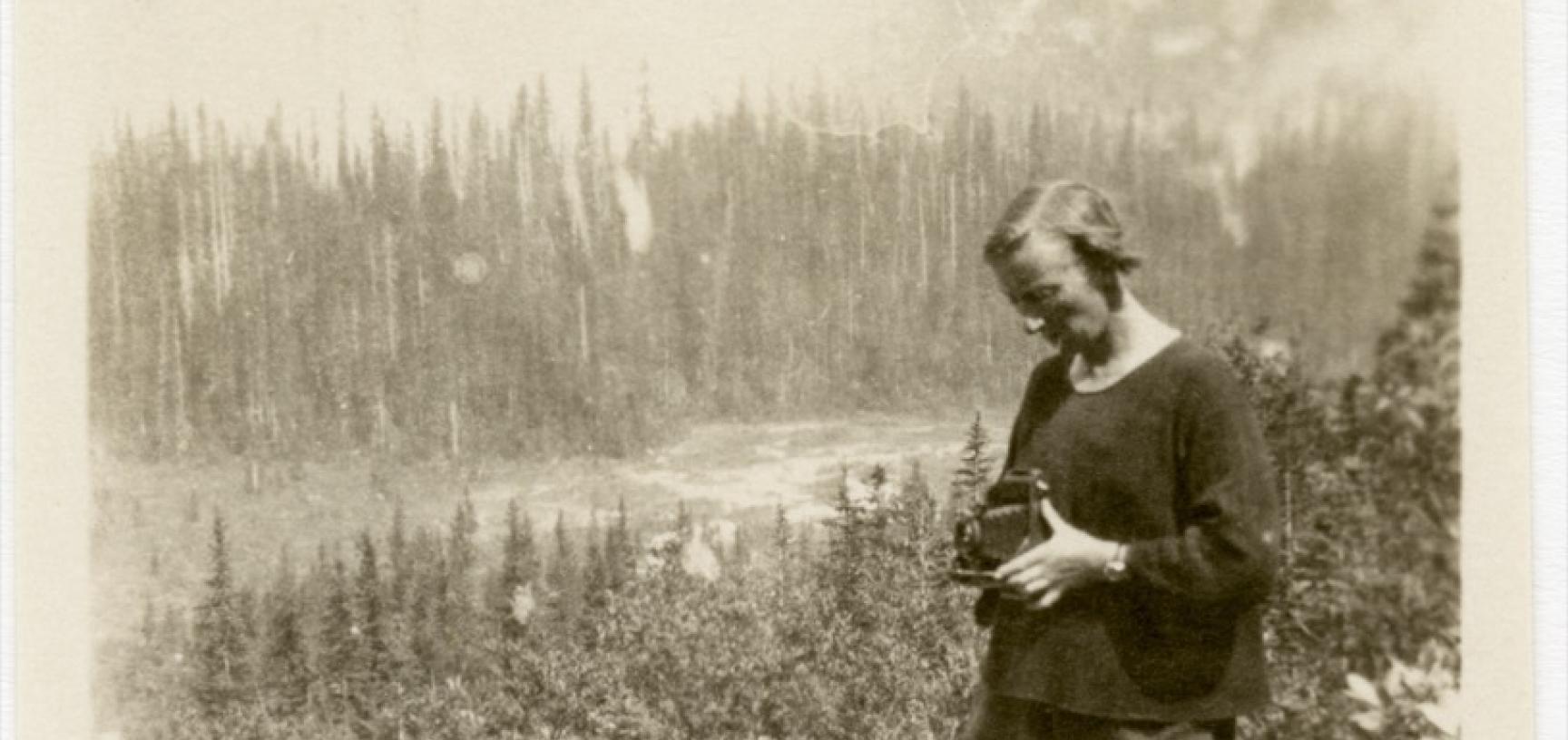 Old photo of a woman taking a photo of a wooded landscape