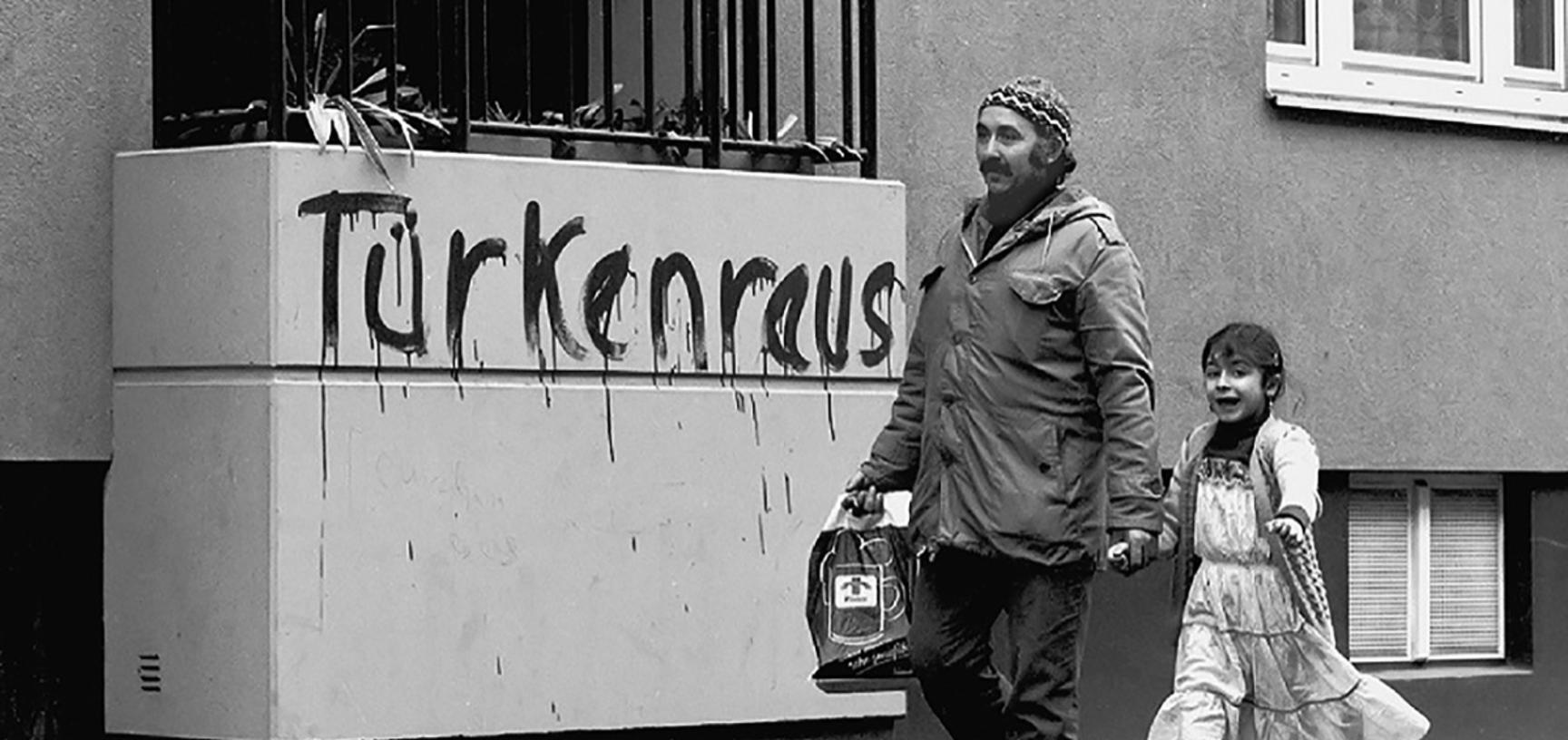 Man and little girl walking past a balcony with "Turkenraus" graffiti