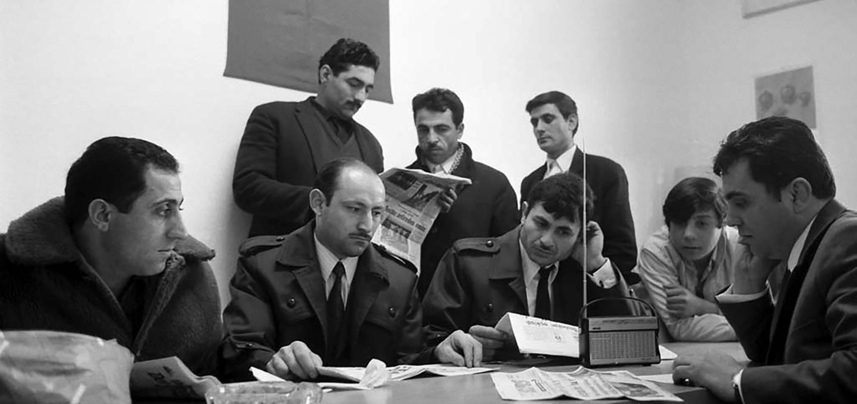 Group of men listening to radio and reading newspapers
