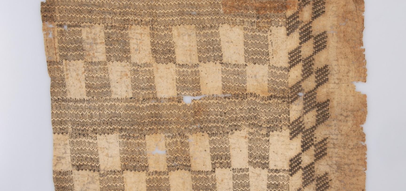 A square piece of light brown fibrous fabric printed with geometric grid patterns in a dark brown ink. 