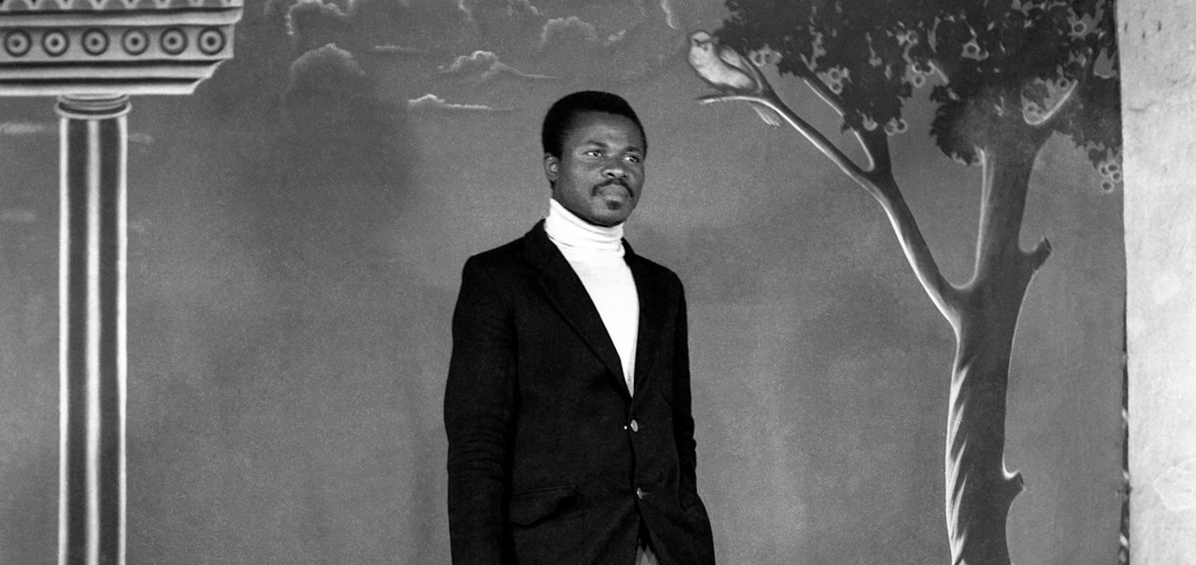 Man with a brief-case standing in front of the photographer’s first painted backdrop, created for Touselle when he established Studio Photo Jacques in 1970. Photograph by Jacques Touselle. Mbouda, Cameroon. Early 1970s.