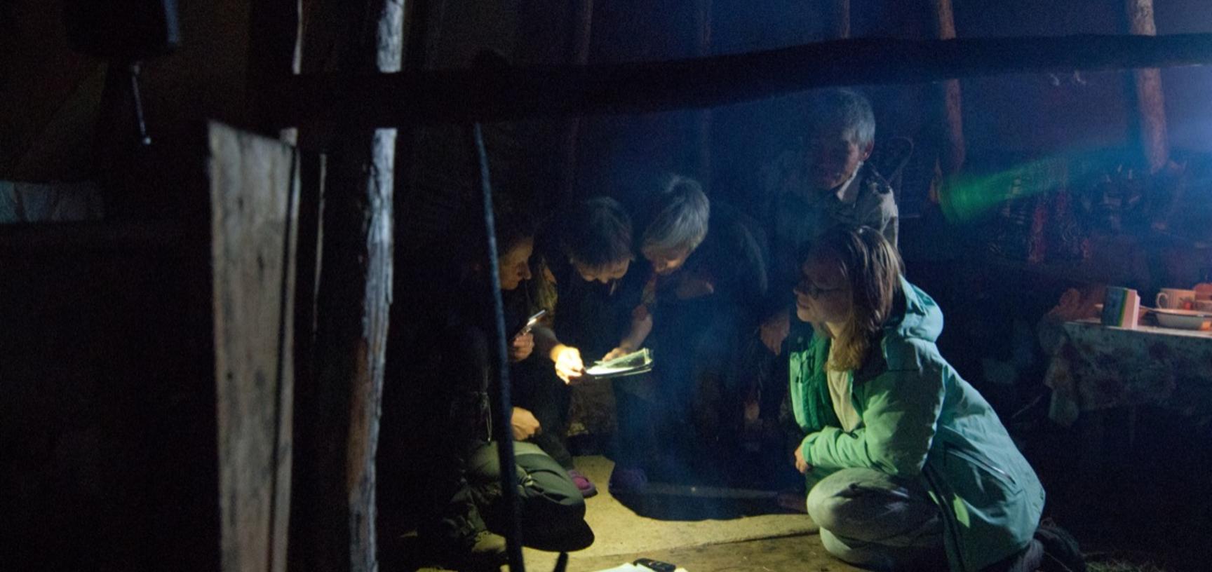 Sharing the digitised Czaplicka collection with Valentina and Nikolay Oyogir, in a dyukcha outside of Chirinda, Evenkia, 2019. Researcher Jaanika Vider leans on the right. Anya Gleizer shines the light from her phone on the left.