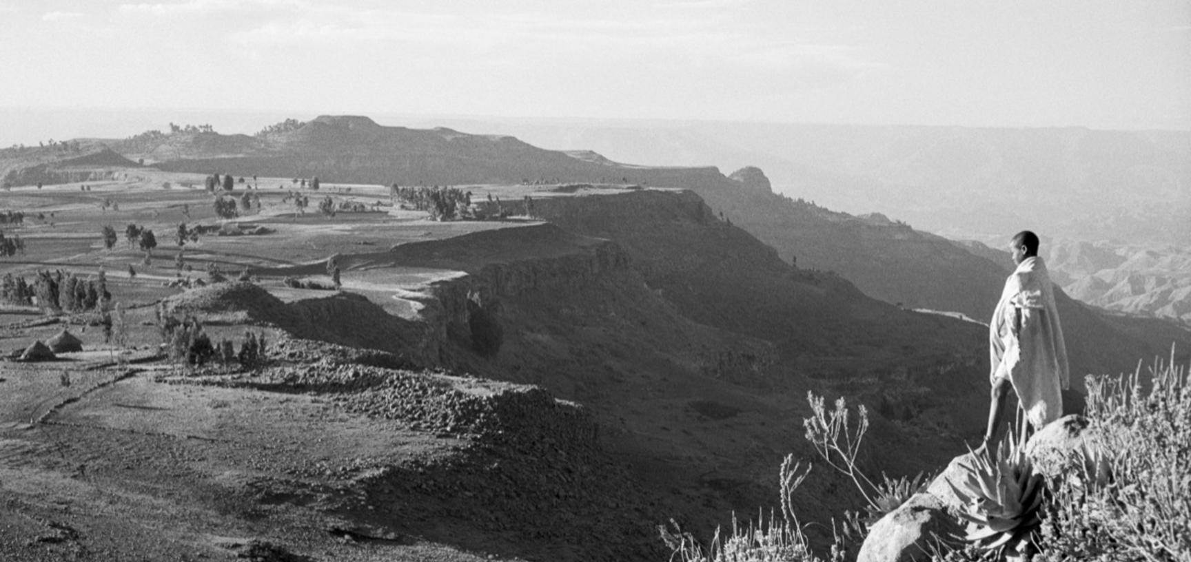 View of an escarpment near Magdala, with a boy standing on rocks in the foreground. Tanta, Ethiopia. Photograph by Wilfred Thesiger. 1960.