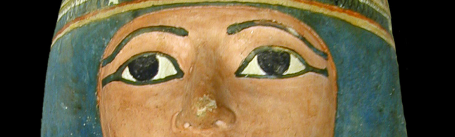 Mummy face with eyes distinctly outlined in black eye liner and a pale indigo wig surrounding the face