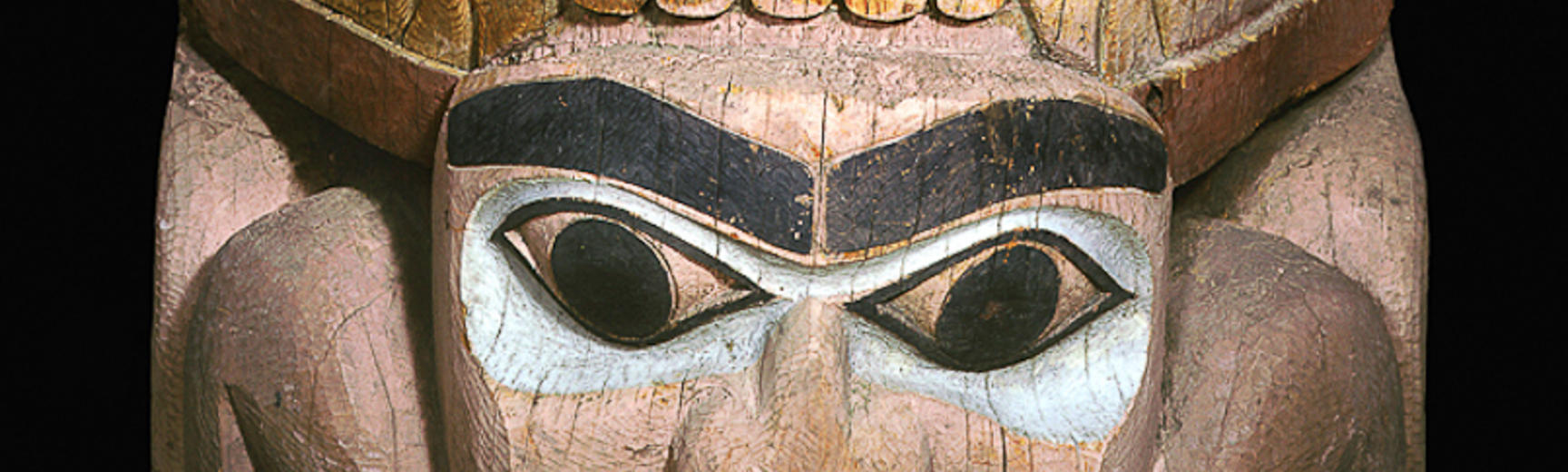 Section of totem pole showing a stylised bear’s face above a man’s face.