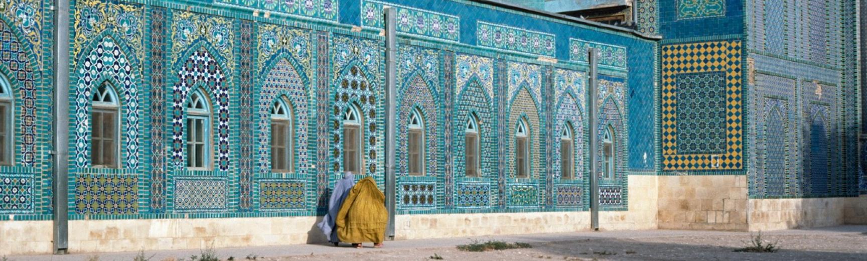 Two women in burqas walking near a brightly decorated blue mosque