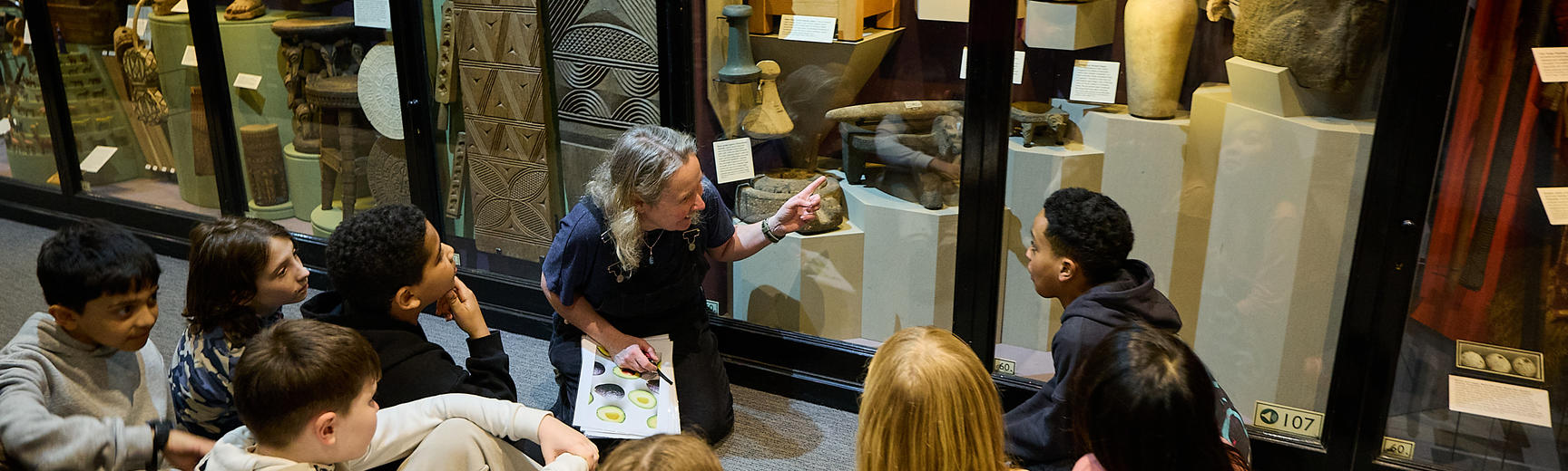 School group sitting on floor looking at case display