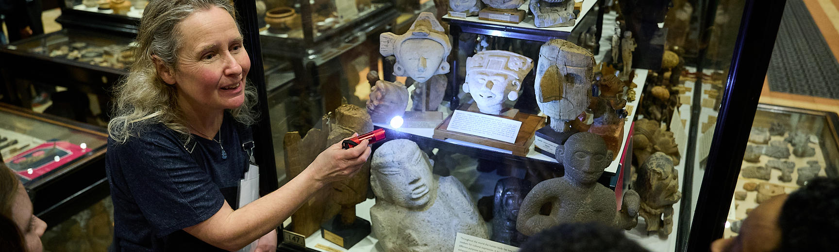 Education officer shining torch into museum case display to show school group