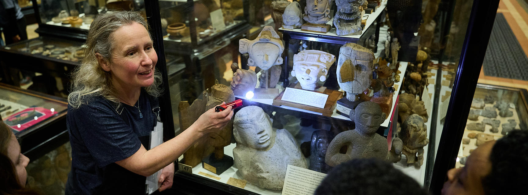 Education officer shining torch into museum case display to show school group