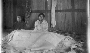 Women with coffin of a child, covered in funerary wrappings. 
