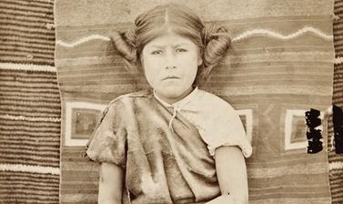 Portrait of a thirteen-year-old Hopi girl named ‘Modisi’, pictured sitting in front of a Navajo blanket. 