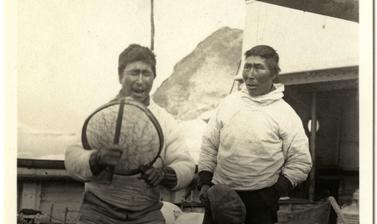 Two Inuit men perform with a drum on the deck of the Quest. Photograph by Henry Iliffe Cozens. Greenland. 1930–1931.