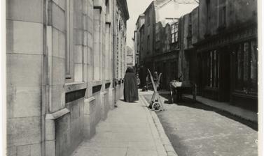 Woman walking in an empty street, wearing a gown with hood for head.