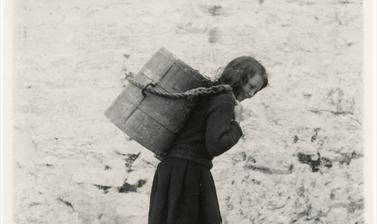 Young girl carrying a tankard of water from the well. 
