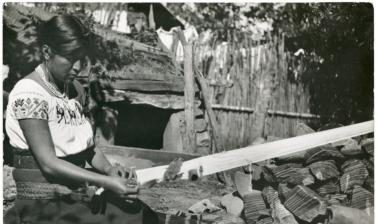 A kneeling woman picking up a gauze pattern on a loom