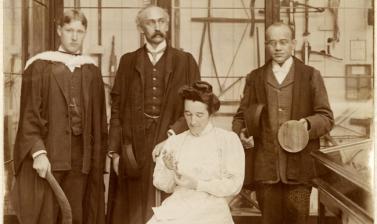 Group portrait of three standing men and a seated woman in an exhibition space