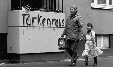 Man and little girl walking past a balcony with "Turkenraus" graffiti