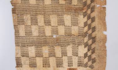 A square piece of light brown fibrous fabric printed with geometric grid patterns in a dark brown ink. 