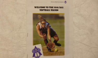 White poster with image of woman playing softball, black text and purple Amazons team logo. 