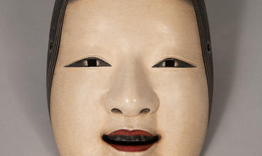 A carved and painted wooden Noh mask depicting a young woman with a light complexion, the mouth slightly open with the lips painted red, including shaved and repainted eyebrows.
