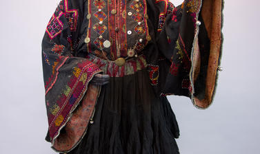 Dress on a mannequin with the left arm raised up and the right arm positioned at the waist, the dress is black stitched with multi-coloured embroidery on the bodice