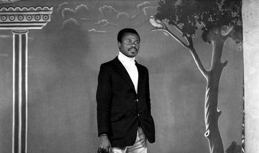 Man with a brief-case standing in front of the photographer’s first painted backdrop, created for Touselle when he established Studio Photo Jacques in 1970. Photograph by Jacques Touselle. Mbouda, Cameroon. Early 1970s.