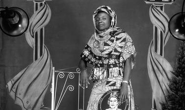 Woman wearing a dress made from fabric printed with Union flags, royal insignia and a circular portrait of Queen Elizabeth II, possibly marking the Queen’s Silver Jubilee. Photograph by Jacques Touselle. Mbouda, Cameroon. About 1977.