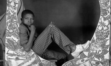 Boy sitting with a painted studio prop: ‘Bonne Année Studio Photo Jacques’. Photograph by Jacques Touselle. Mbouda, Cameroon. About 1975.