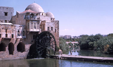 A waterwheel attached to a building rotates over a river.  