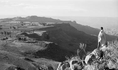 View of an escarpment near Magdala, with a boy standing on rocks in the foreground. Tanta, Ethiopia. Photograph by Wilfred Thesiger. 1960.