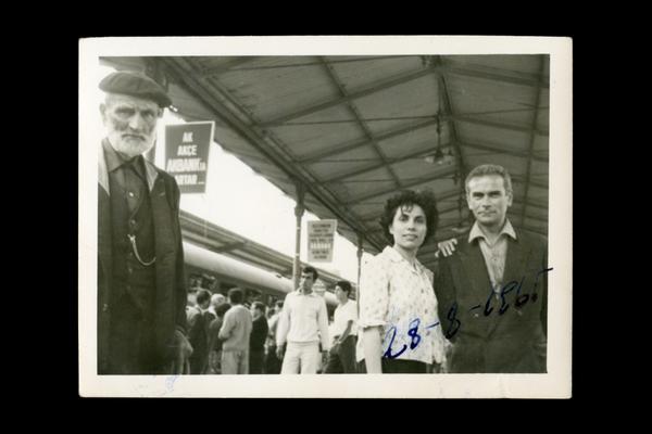 A couple and an old man posing on a crowded railway platform