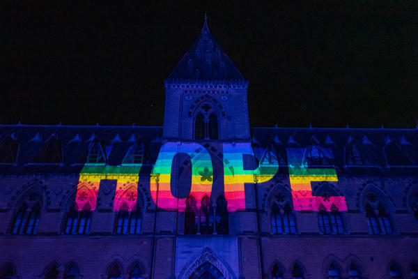Rainbow letters spelling Hope projected onto dark front of Museum of Natural History