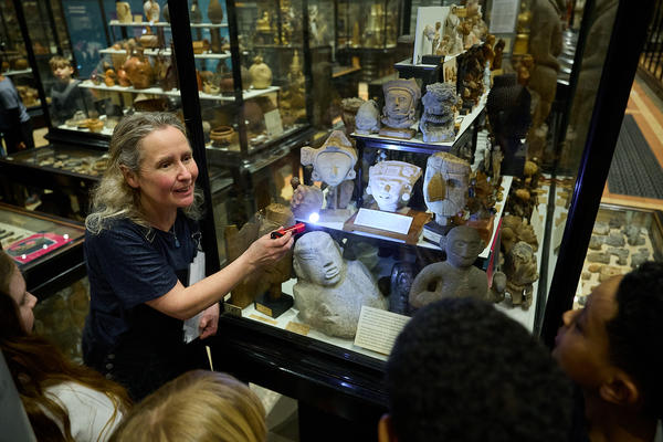 Education officer shining torch into museum case display to show school group