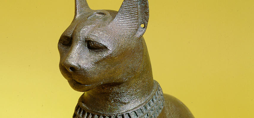 Large bronze seated cat with inlaid collar and pendant, mounted on a wooden stand, representing the goddess Bast.