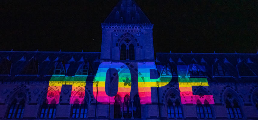Rainbow letters spelling Hope projected onto dark front of Museum of Natural History