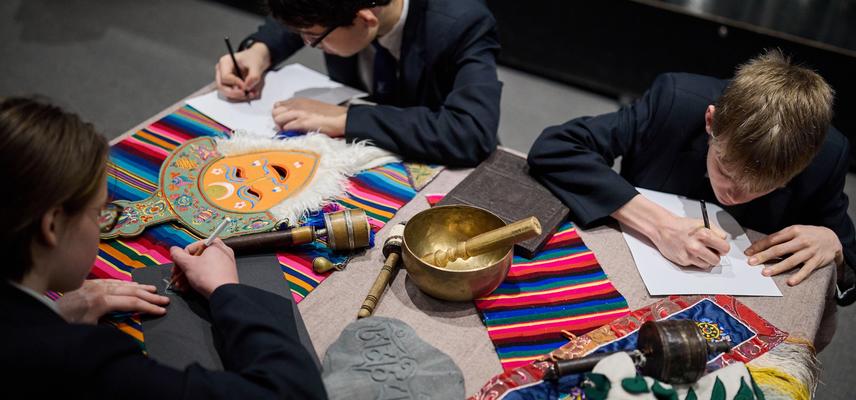 School students sitting around a table drawing colourful objects laid out on the table.
