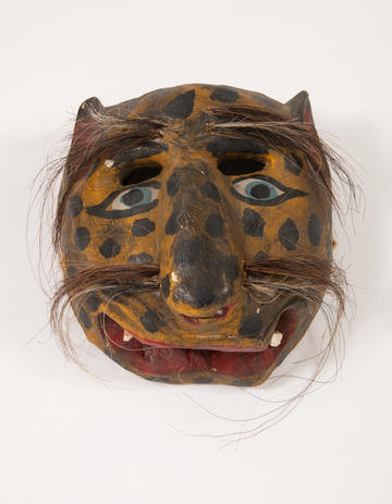 Painted wooden animal mask with dotted checks and hairy eyebrows and whiskers