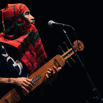 Musician wearing red embroidered hood playing tonkori