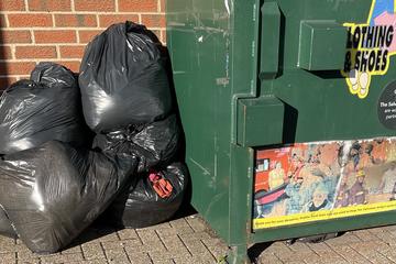 Recycling bin with black rubbish bags piled up next to it