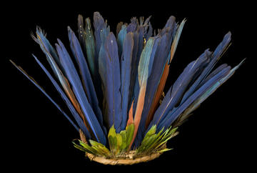 Feathered headdress with long blue feathers set behind short green feathers in wicker base.