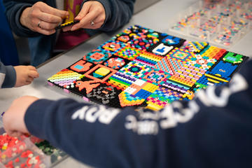 Close up of arm and pair of hands assembling a colourful pattern of plastic bricks